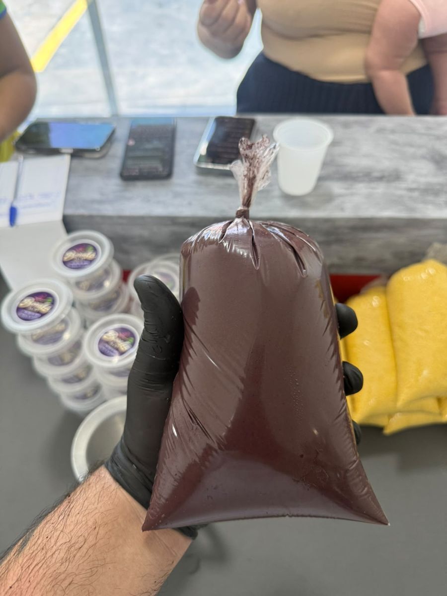 Saco de açaí fechado na mão do atendente, com potes da marca ao fundo